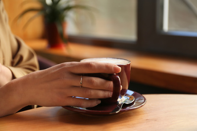 Photo of Woman with aromatic coffee at table in cafe, closeup