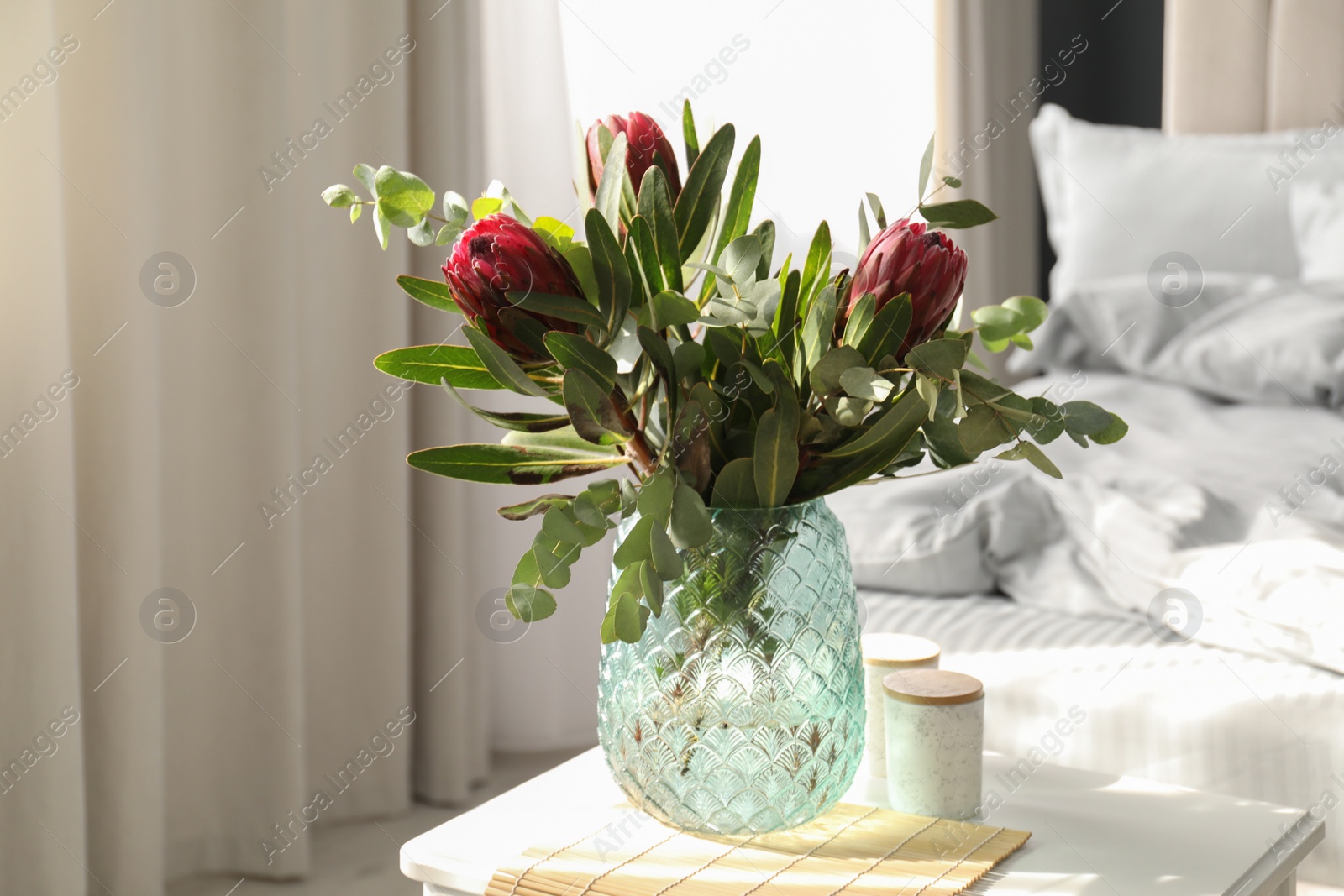 Vase with bouquet of beautiful Protea flowers on white table in bedroom Photo of Vase with bouquet of beautiful Protea flowers on white table in bedroom