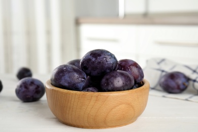 Delicious ripe plums in wooden bowl on white table Photo of Delicious ripe plums in wooden bowl on white table