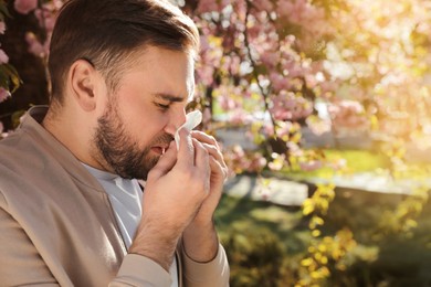 Man suffering from seasonal pollen allergy near blossoming tree outdoors Photo of Man suffering from seasonal pollen allergy near blossoming tree outdoors