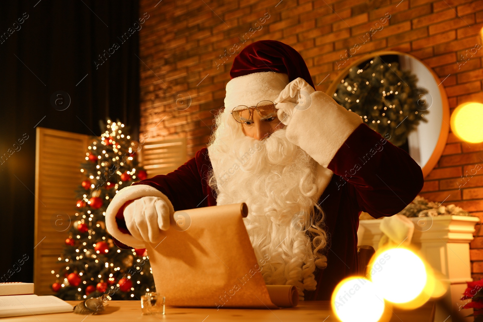 Santa Claus reading wish list at table indoors Photo of Santa Claus reading wish list at table indoors