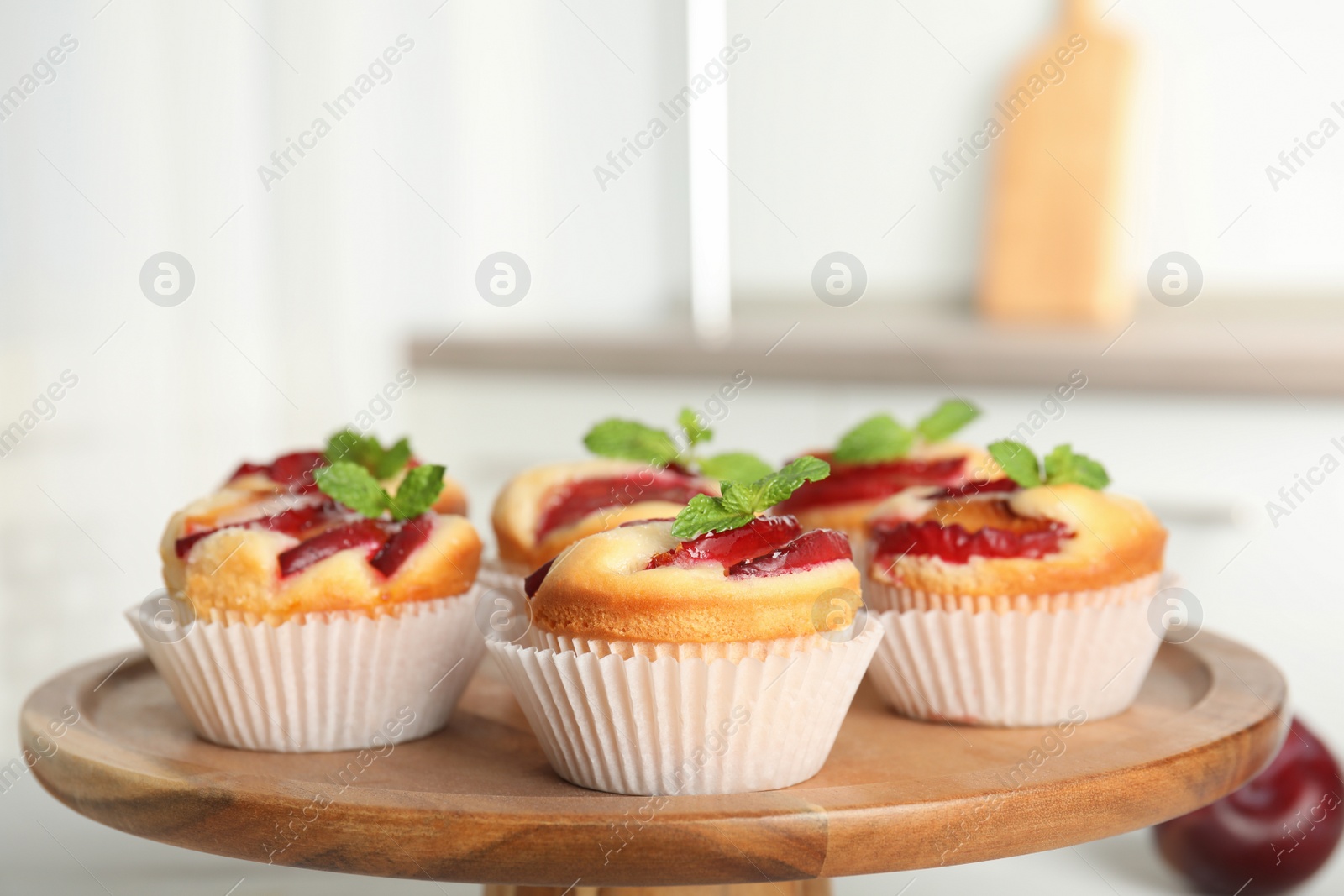 Delicious sweet cupcakes with plums on wooden stand, closeup Photo of Delicious sweet cupcakes with plums on wooden stand, closeup