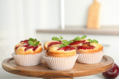 Delicious sweet cupcakes with plums on wooden stand, closeup Photo of Delicious sweet cupcakes with plums on wooden stand, closeup