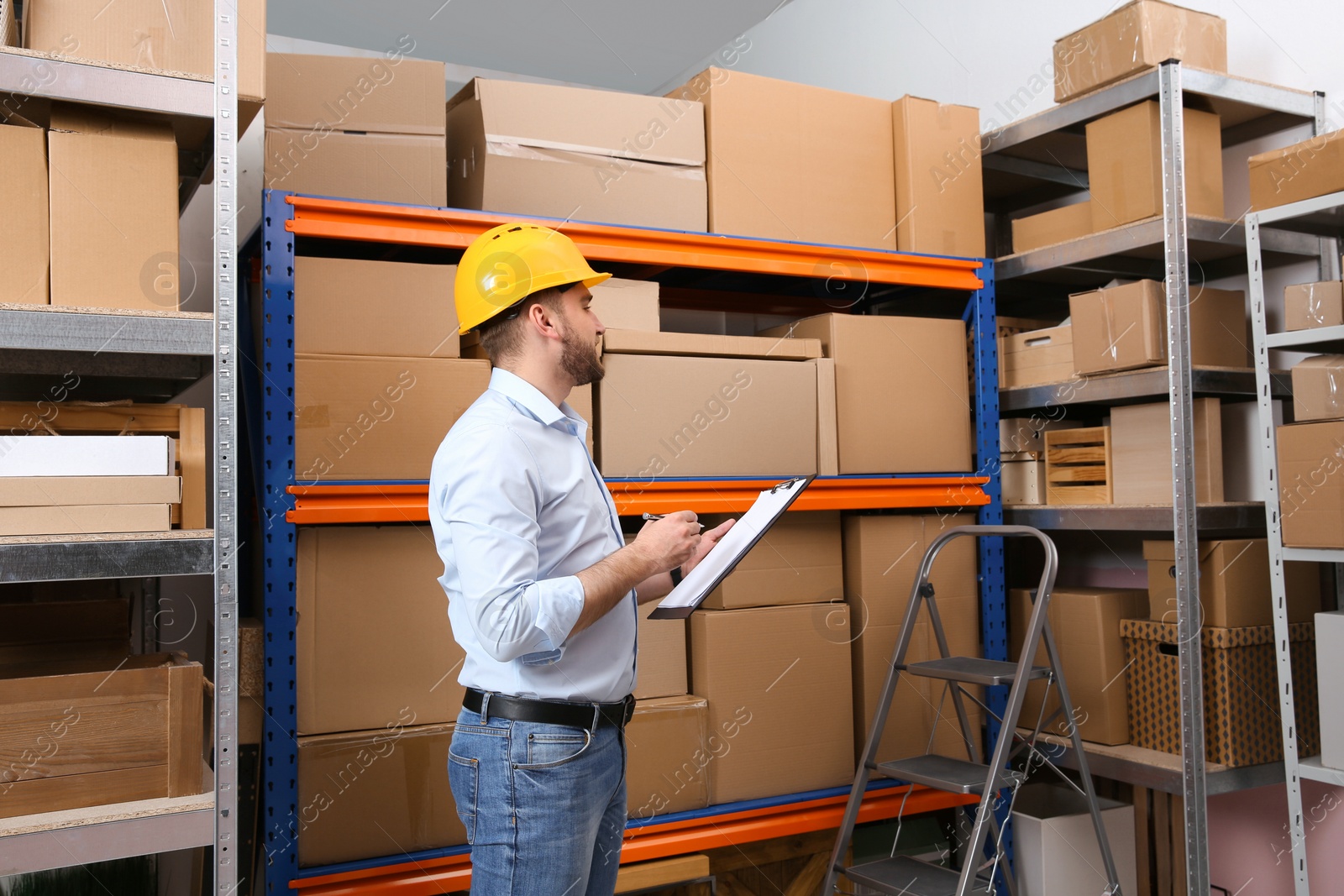 Young man with clipboard near rack of cardboard boxes at warehouse Photo of Young man with clipboard near rack of cardboard boxes at warehouse