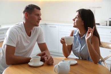 Man and woman talking while drinking tea at table in kitchen Photo of Man and woman talking while drinking tea at table in kitchen