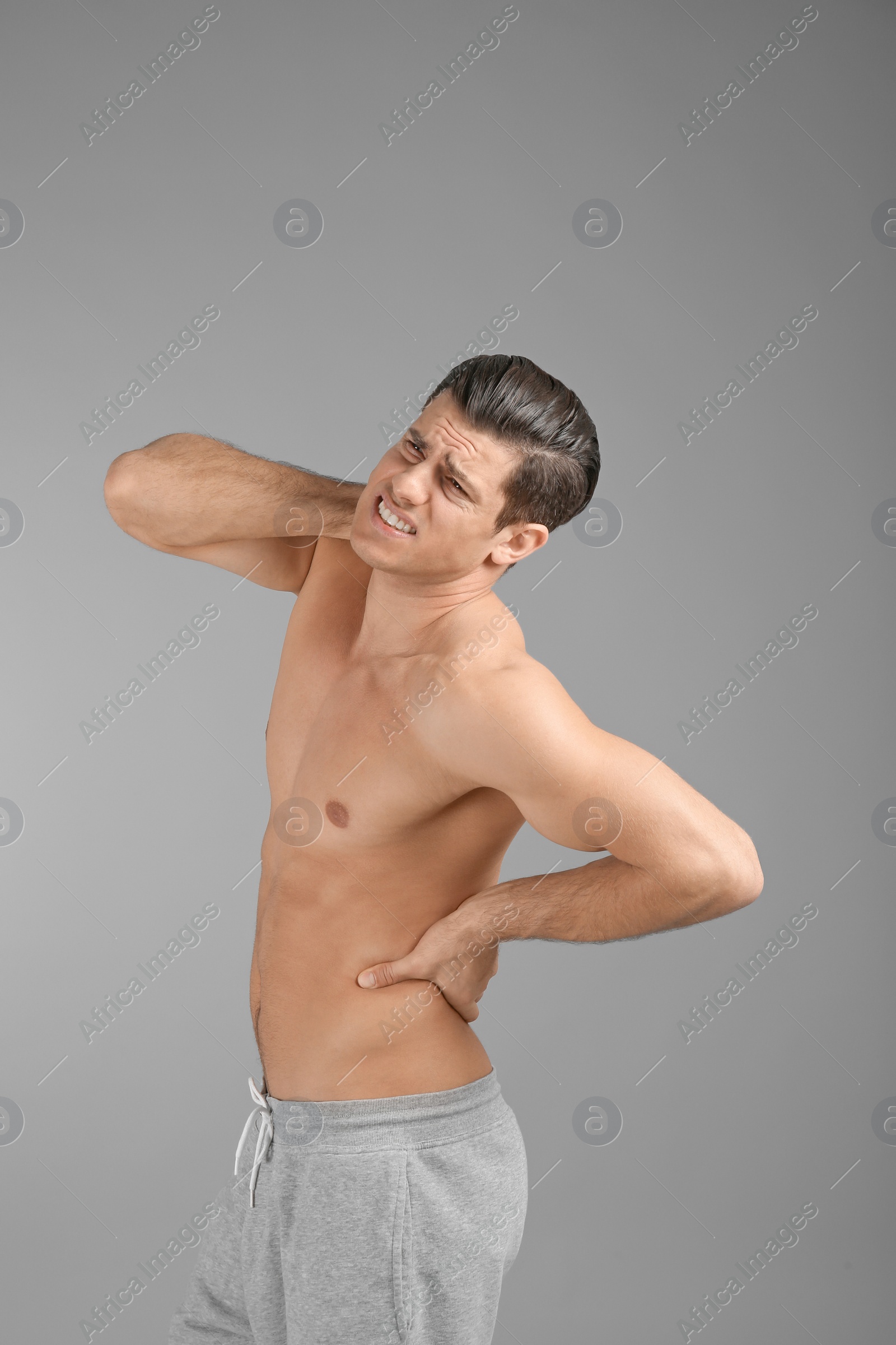 Young man suffering from back pain on grey background Photo of Young man suffering from back pain on grey background