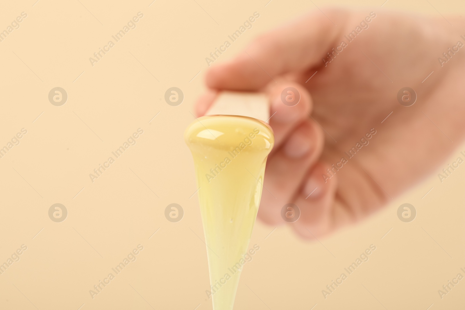 Woman holding spatula with hot depilatory wax on beige background, closeup Photo of Woman holding spatula with hot depilatory wax on beige background, closeup