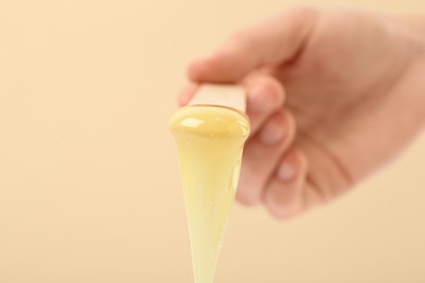 Woman holding spatula with hot depilatory wax on beige background, closeup Photo of Woman holding spatula with hot depilatory wax on beige background, closeup
