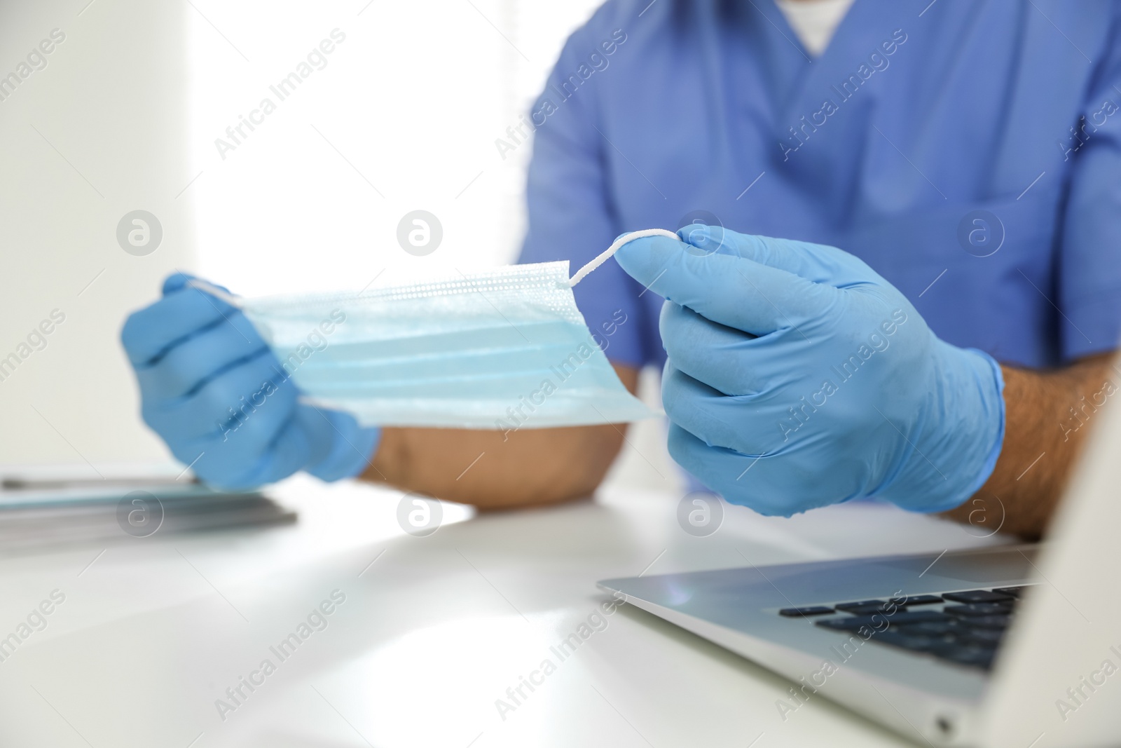 Doctor in medical gloves holding protective mask at table in office, closeup Photo of Doctor in medical gloves holding protective mask at table in office, closeup