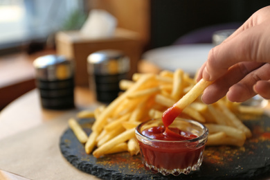 Woman dipping French fries into red sauce in cafe, closeup Photo of Woman dipping French fries into red sauce in cafe, closeup