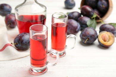 Delicious plum liquor and ripe fruits on white wooden table, closeup. Homemade strong alcoholic beverage Photo of Delicious plum liquor and ripe fruits on white wooden table, closeup. Homemade strong alcoholic beverage