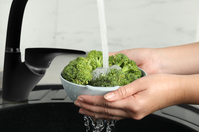 Woman washing fresh green broccoli in kitchen sink, closeup Photo of Woman washing fresh green broccoli in kitchen sink, closeup