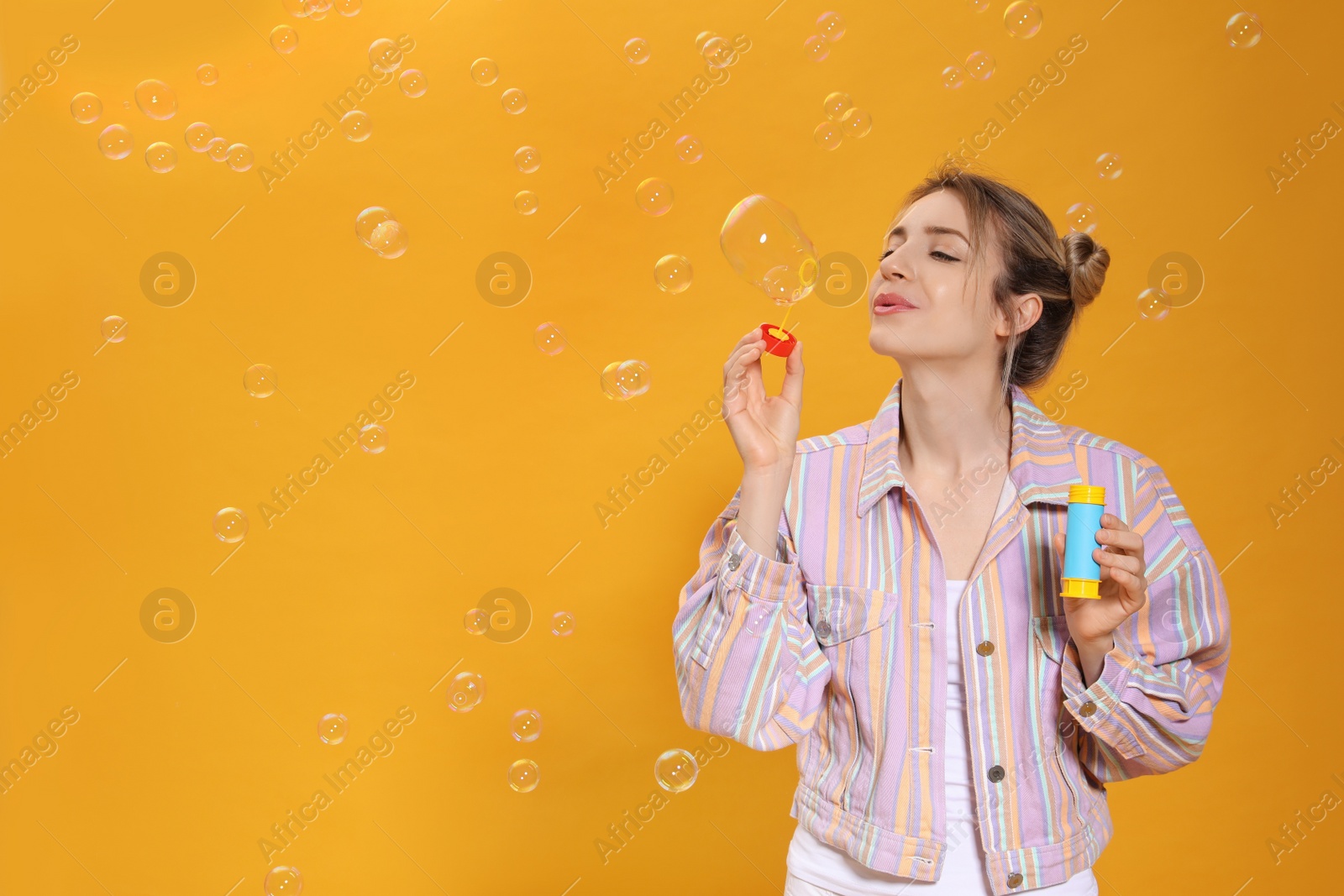 Young woman blowing soap bubbles on yellow background, space for text Photo of Young woman blowing soap bubbles on yellow background, space for text