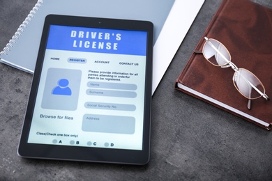 Tablet with driver's license application form, glasses and stationery on grey table Photo of Tablet with driver's license application form, glasses and stationery on grey table