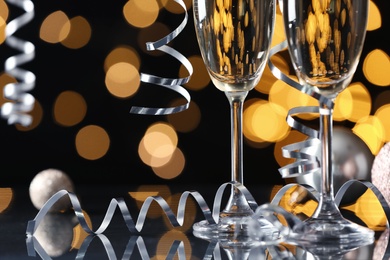 Glasses of champagne, Christmas decor and serpentine streamers against black background with blurred lights, closeup. Space for text Photo of Glasses of champagne, Christmas decor and serpentine streamers against black background with blurred lights, closeup. Space for text