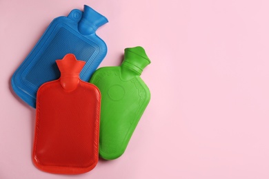 Photo of Hot water bottles on pink background, flat lay. Space for text