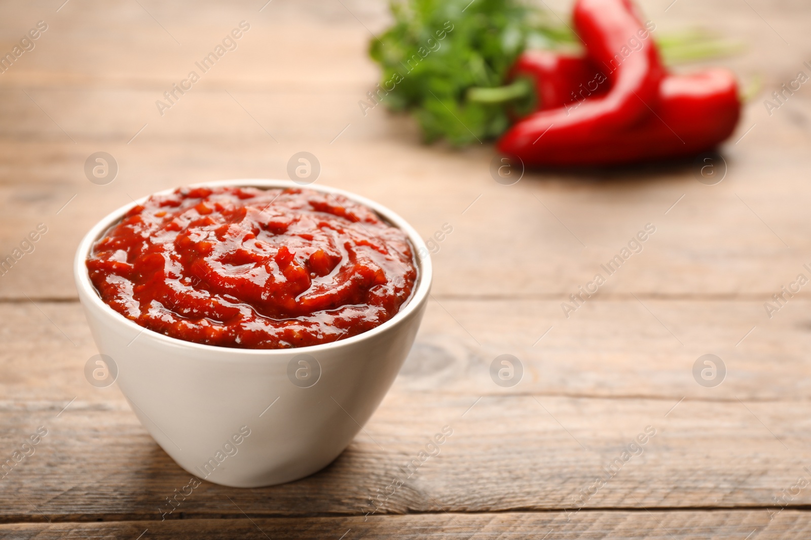 Delicious adjika sauce in bowl on wooden table, closeup. Space for text Photo of Delicious adjika sauce in bowl on wooden table, closeup. Space for text