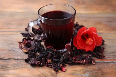 Delicious hibiscus tea and dry flowers on wooden table Photo of Delicious hibiscus tea and dry flowers on wooden table