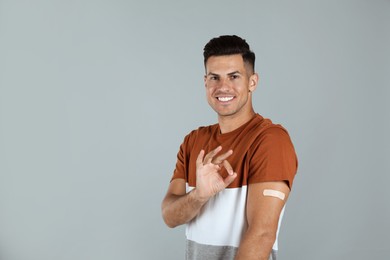Vaccinated man with medical plaster on his arm showing okay gesture against grey background Photo of Vaccinated man with medical plaster on his arm showing okay gesture against grey background