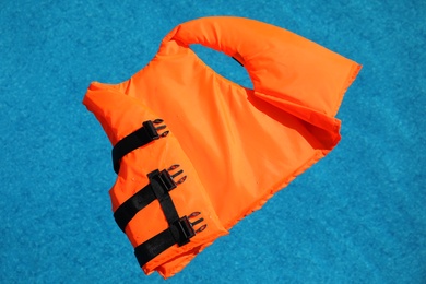 Bright orange life jacket floating in swimming pool, top view Photo of Bright orange life jacket floating in swimming pool, top view
