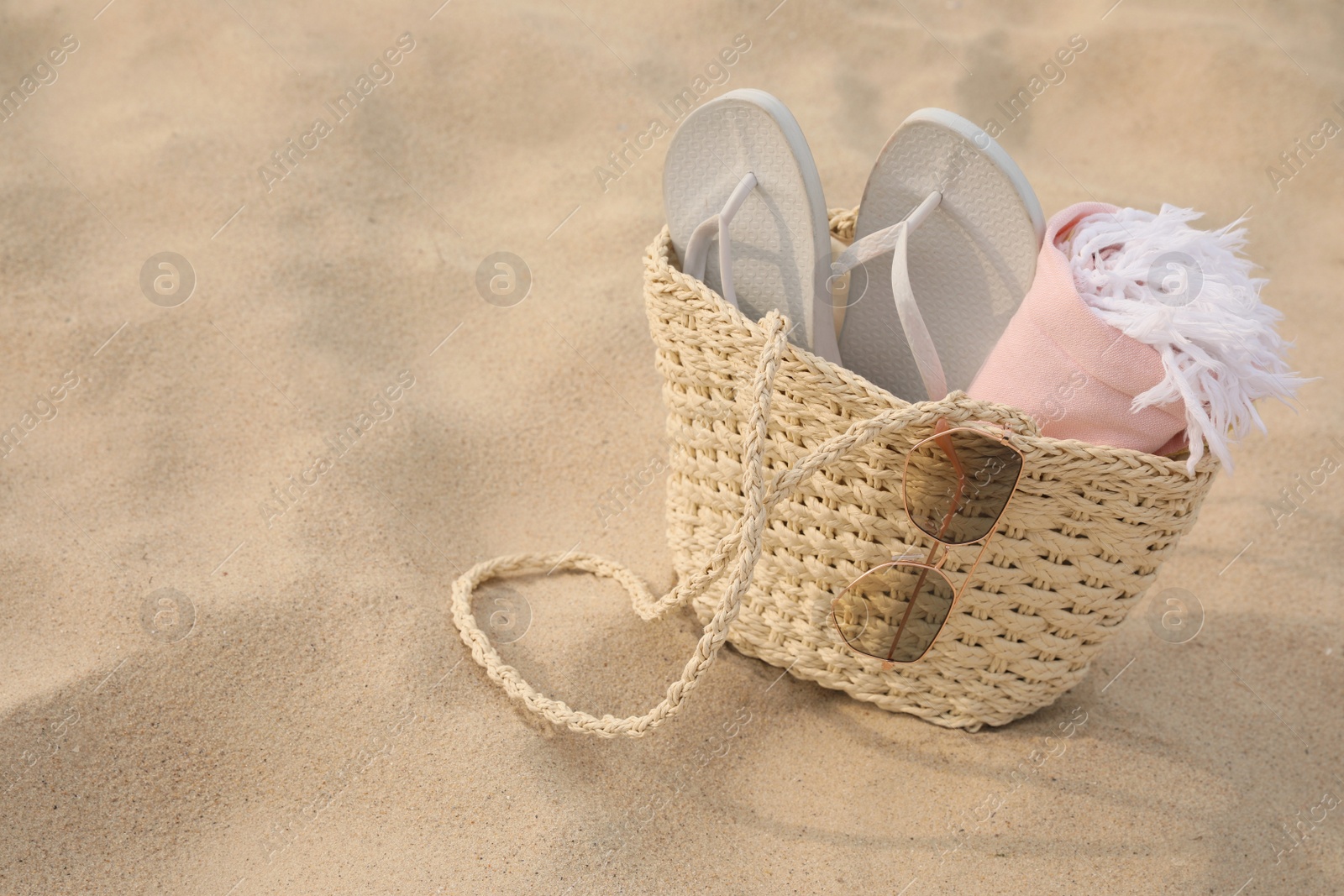 Photo of Beach bag with flip flops, towel and sunglasses on sand, space for text