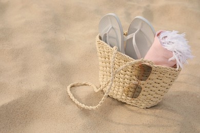 Photo of Beach bag with flip flops, towel and sunglasses on sand, space for text