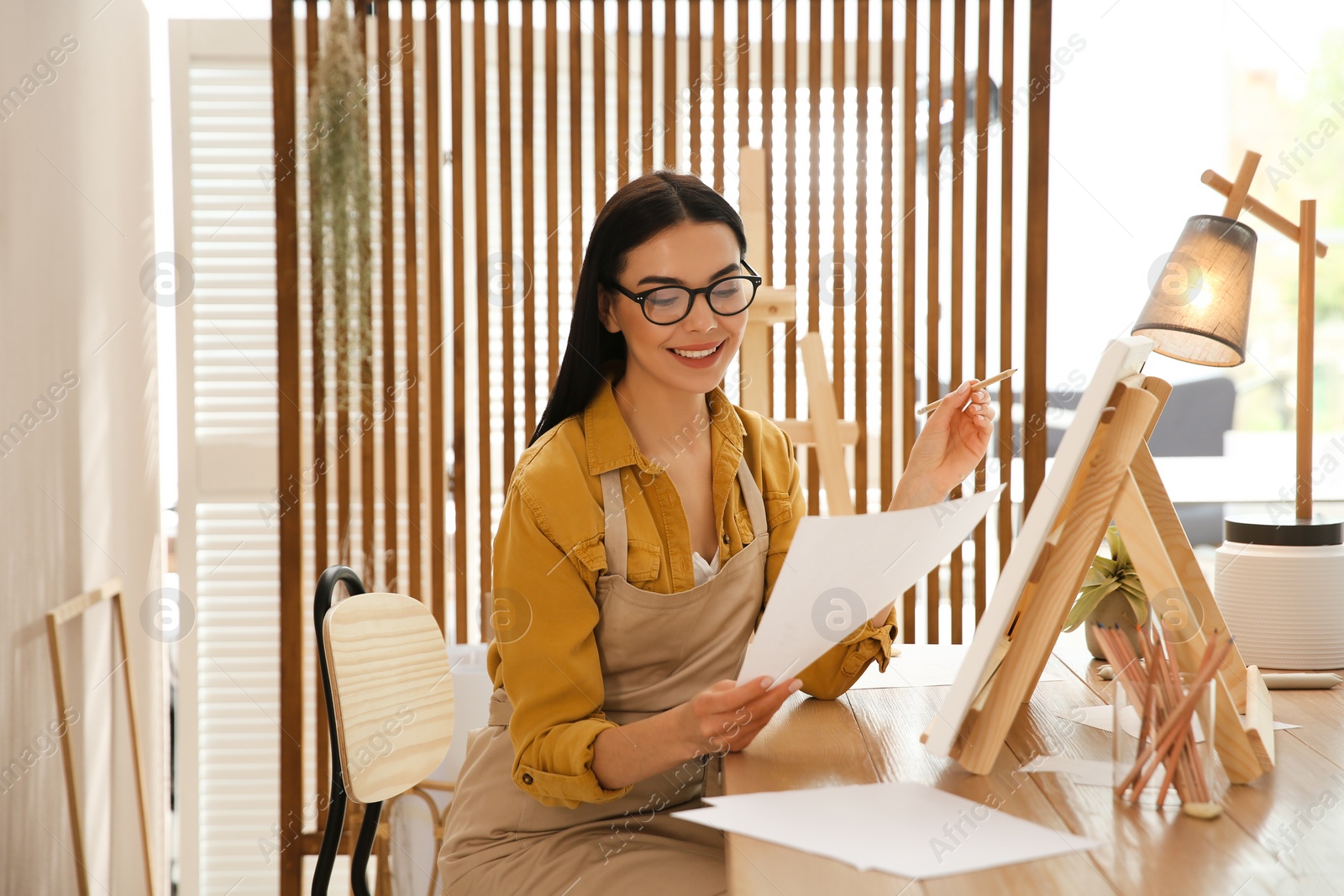 Young woman drawing on easel with pencil at table indoors Photo of Young woman drawing on easel with pencil at table indoors
