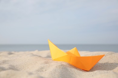 Orange paper boat on sandy beach near sea, space for text Photo of Orange paper boat on sandy beach near sea, space for text