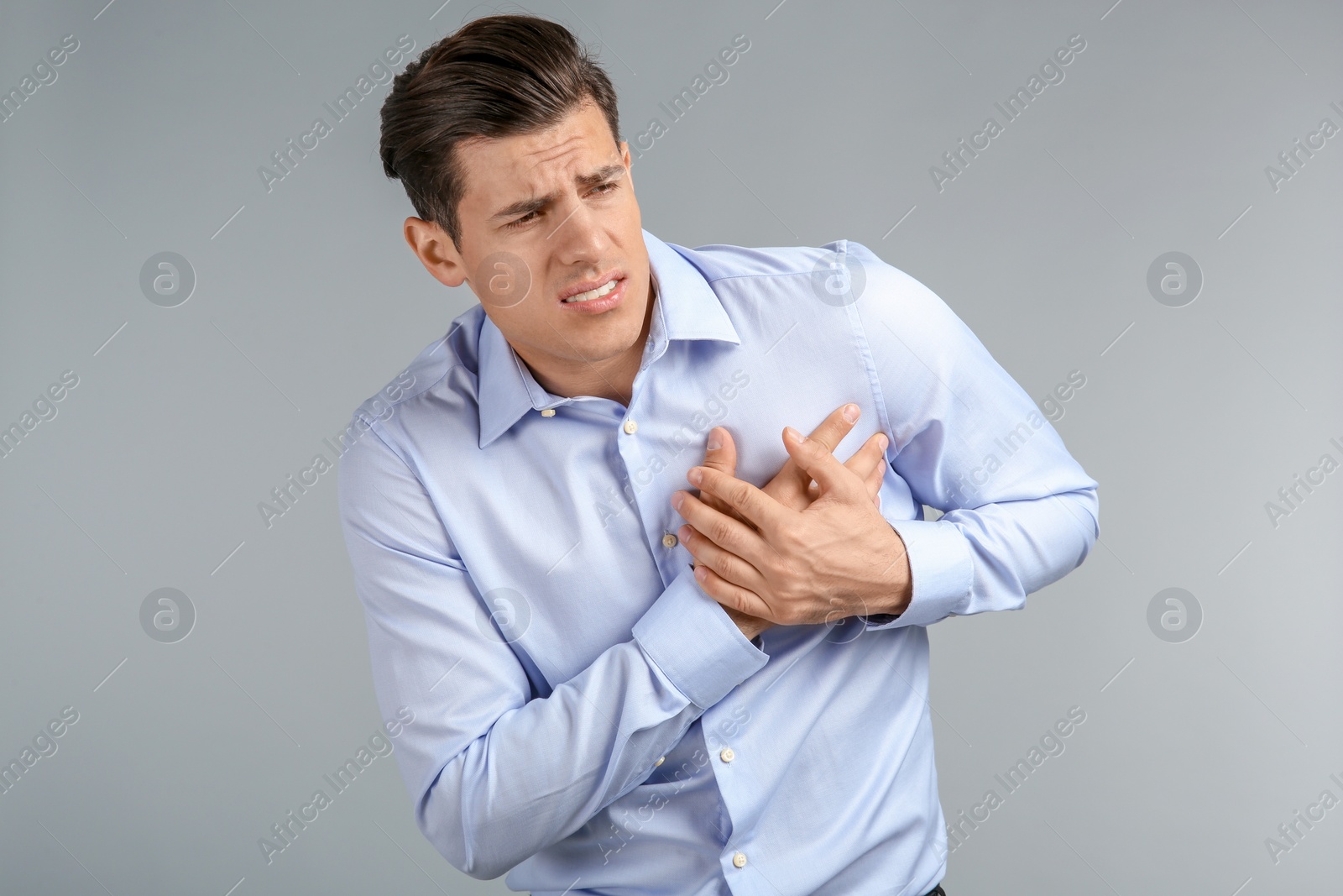 Young man suffering from chest pain on grey background Photo of Young man suffering from chest pain on grey background