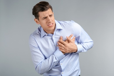 Young man suffering from chest pain on grey background Photo of Young man suffering from chest pain on grey background