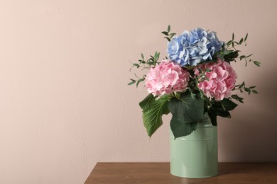 Beautiful hortensia flowers in can on wooden table against beige background. Space for text Photo of Beautiful hortensia flowers in can on wooden table against beige background. Space for text
