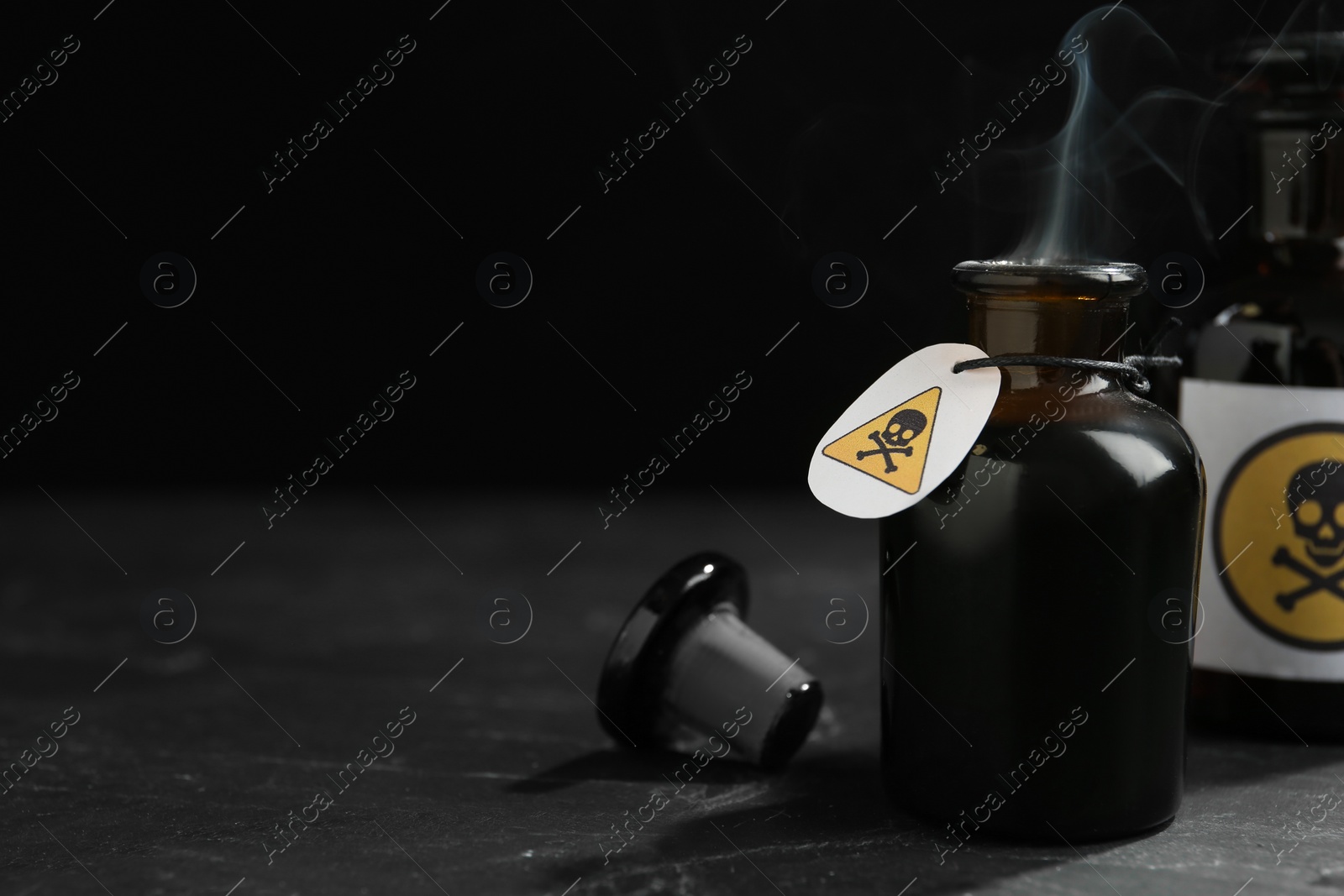 Open glass bottle of smoking poison with warning sign on black table. Space for text Photo of Open glass bottle of smoking poison with warning sign on black table. Space for text