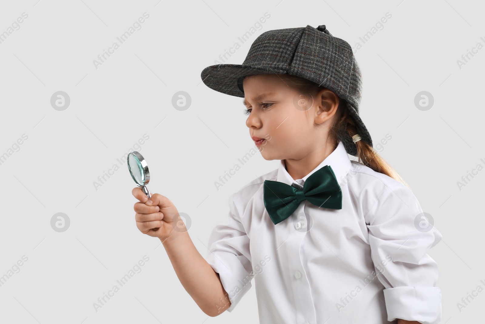 Cute little detective with magnifying glass on grey background Photo of Cute little detective with magnifying glass on grey background