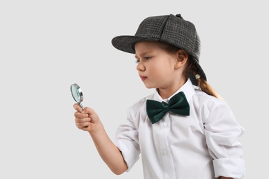 Cute little detective with magnifying glass on grey background Photo of Cute little detective with magnifying glass on grey background