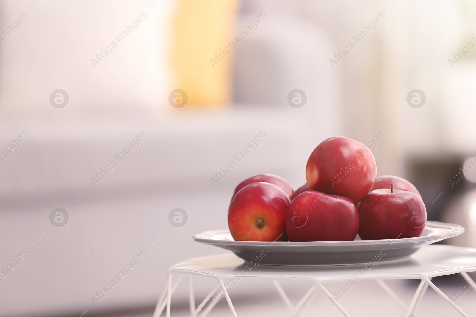 Plate with ripe red apples on table against blurred background Photo of Plate with ripe red apples on table against blurred background