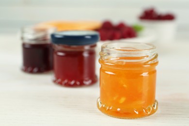 Jars with different sweet jams on white wooden table, closeup. Space for text Photo of Jars with different sweet jams on white wooden table, closeup. Space for text