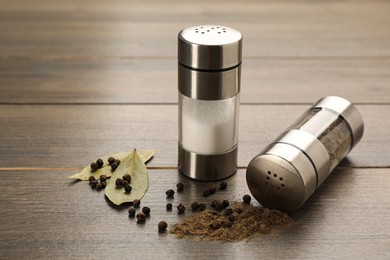 Salt and pepper shakers with bay leaves on wooden table, closeup Photo of Salt and pepper shakers with bay leaves on wooden table, closeup