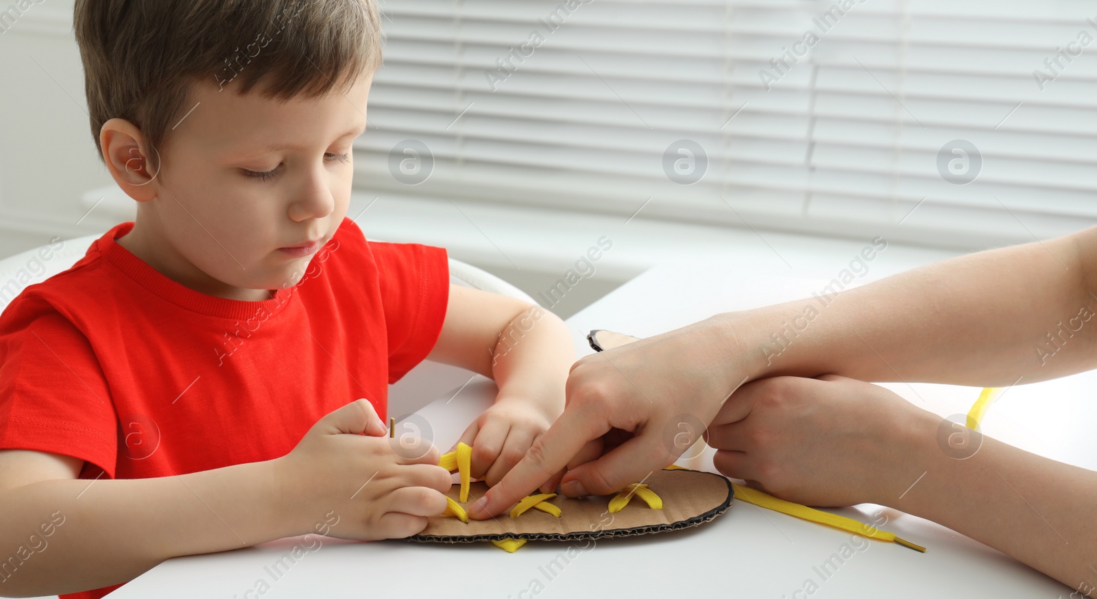Mother teaching son to tie shoe laces using training cardboard template at white table, closeup Photo of Mother teaching son to tie shoe laces using training cardboard template at white table, closeup