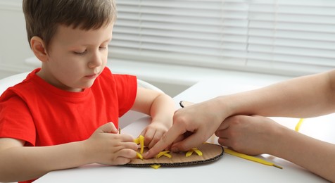 Mother teaching son to tie shoe laces using training cardboard template at white table, closeup Photo of Mother teaching son to tie shoe laces using training cardboard template at white table, closeup