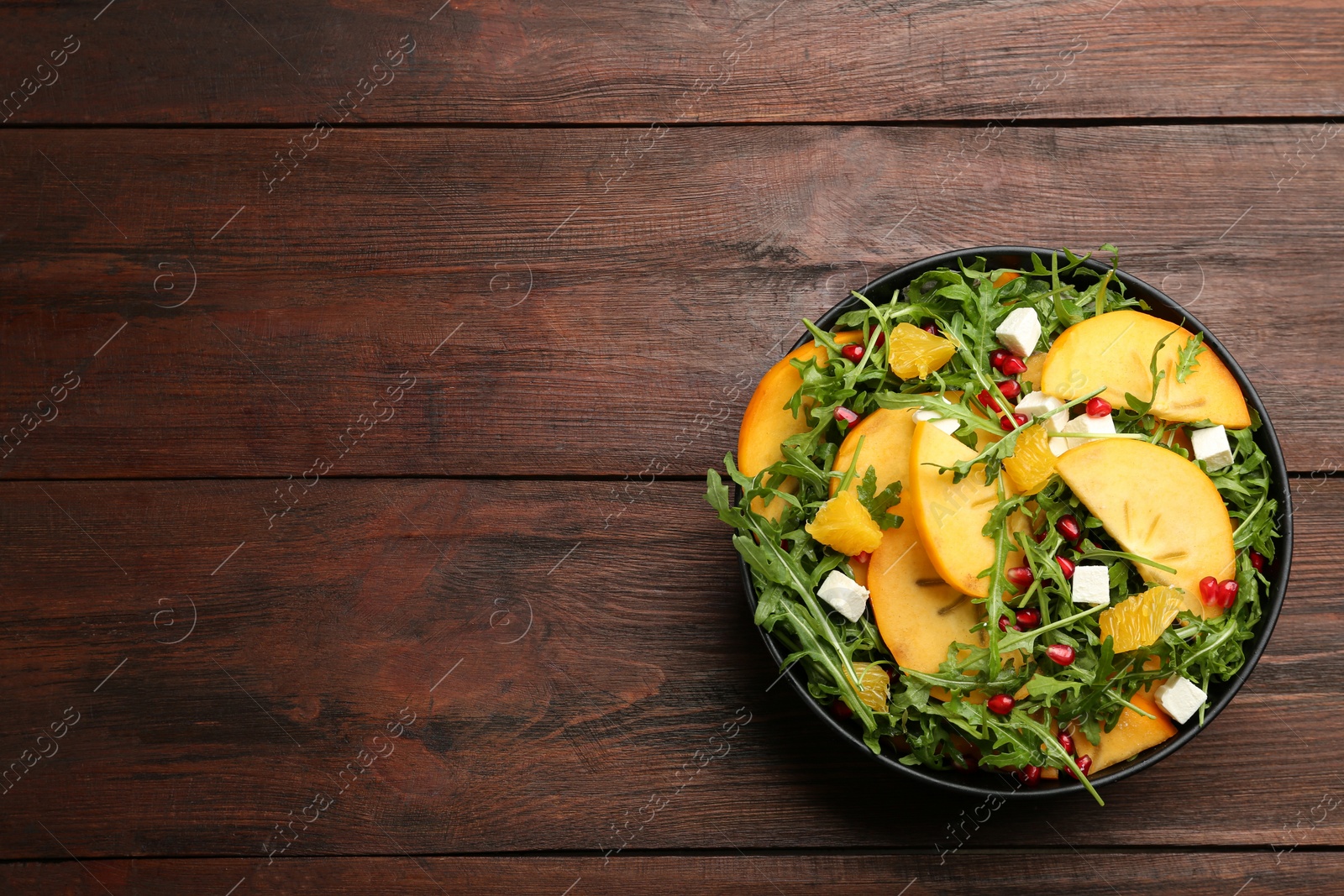 Delicious persimmon salad with pomegranate and arugula on wooden table, top view. Space for text Photo of Delicious persimmon salad with pomegranate and arugula on wooden table, top view. Space for text