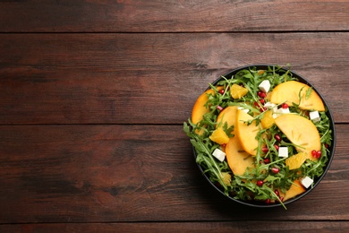 Delicious persimmon salad with pomegranate and arugula on wooden table, top view. Space for text Photo of Delicious persimmon salad with pomegranate and arugula on wooden table, top view. Space for text