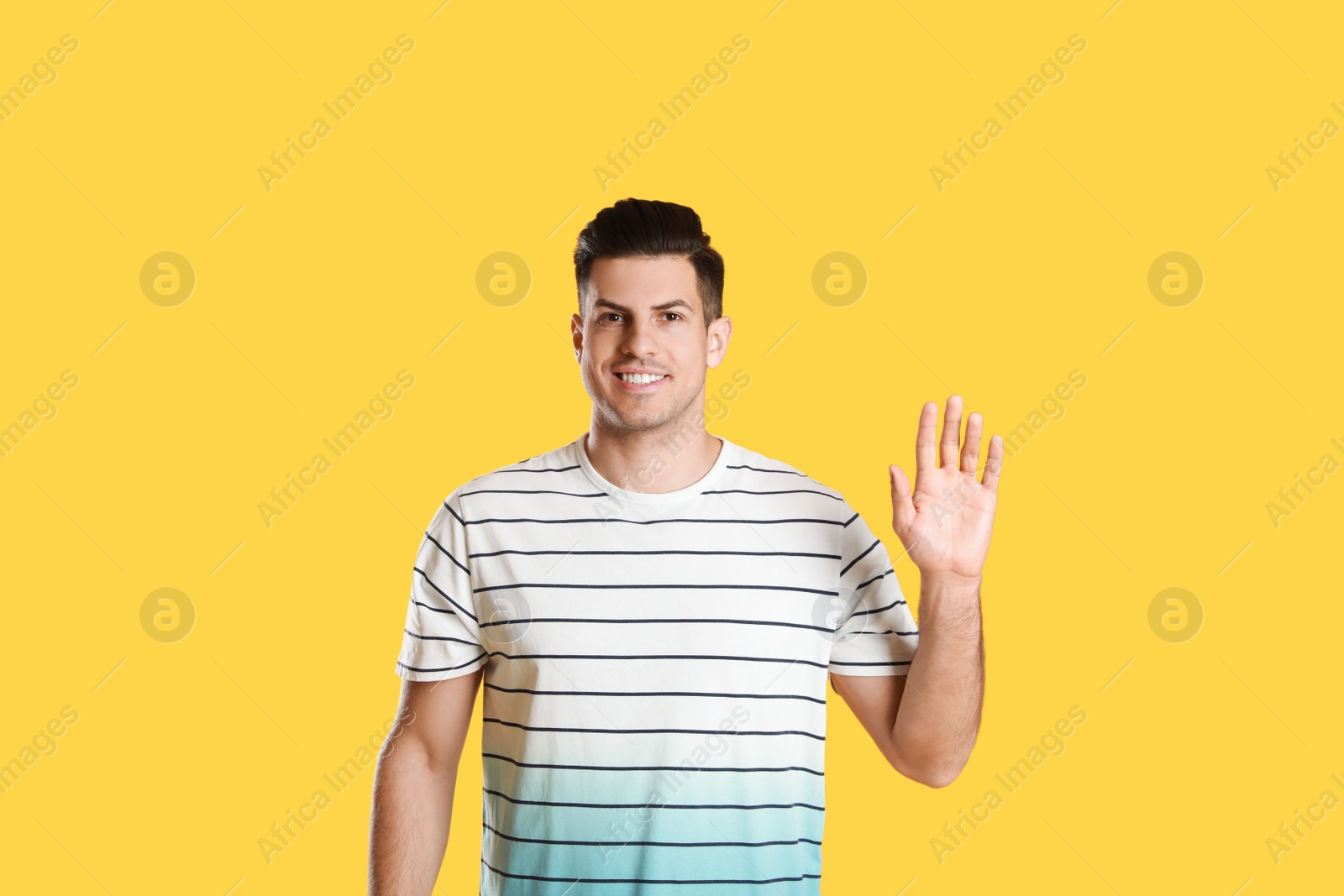 Cheerful man waving to say hello on yellow background Photo of Cheerful man waving to say hello on yellow background