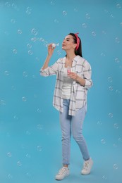 Young woman blowing soap bubbles on light blue background Photo of Young woman blowing soap bubbles on light blue background