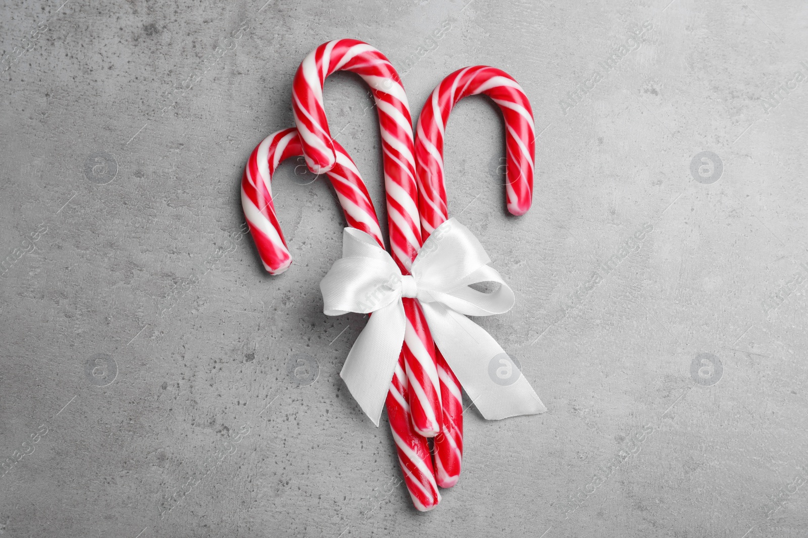 Sweet Christmas candy canes with white bow on grey background, top view Photo of Sweet Christmas candy canes with white bow on grey background, top view