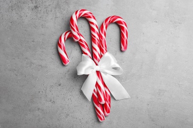 Sweet Christmas candy canes with white bow on grey background, top view Photo of Sweet Christmas candy canes with white bow on grey background, top view