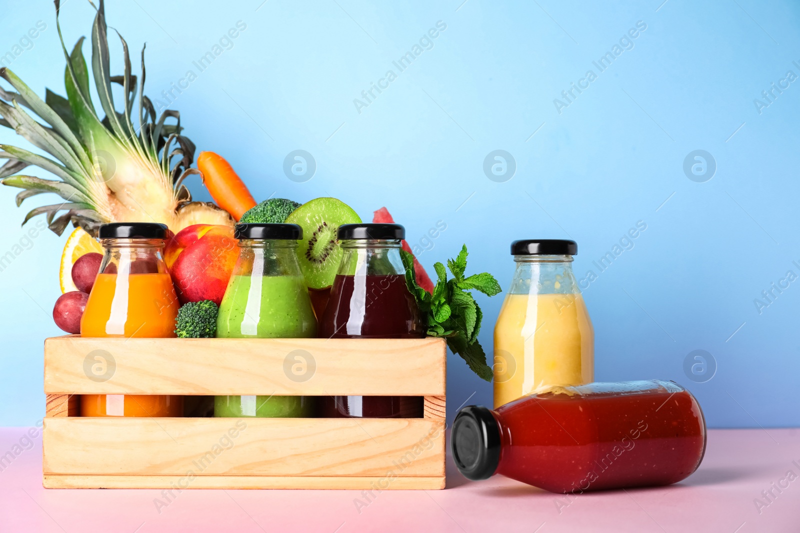 Bottles with delicious colorful juices and fresh ingredients in wooden crate on pink table Photo of Bottles with delicious colorful juices and fresh ingredients in wooden crate on pink table