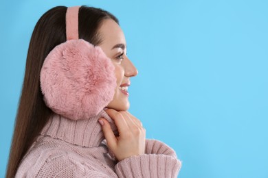Photo of Beautiful young woman wearing earmuffs on light blue background. Space for text