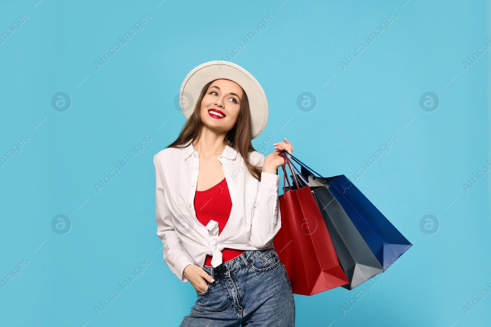 Stylish young woman with shopping bags on light blue background Photo of Stylish young woman with shopping bags on light blue background