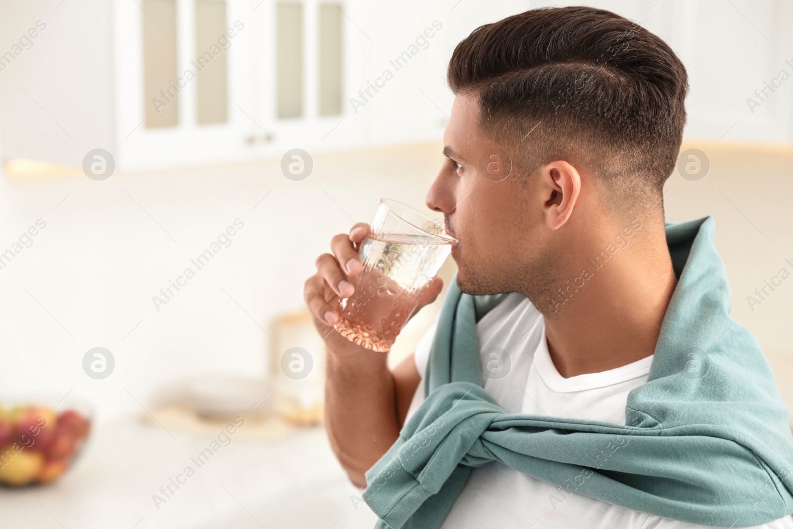 Man drinking pure water from glass in kitchen. Space for text Photo of Man drinking pure water from glass in kitchen. Space for text