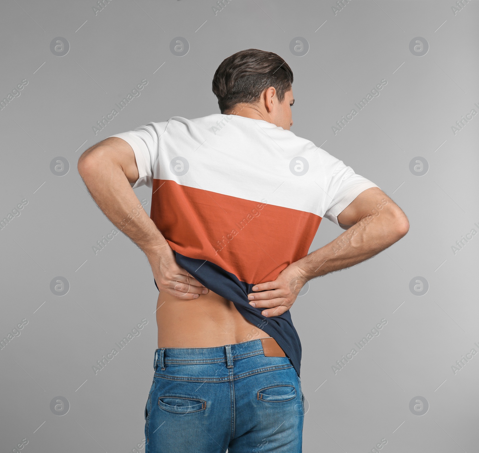 Young man suffering from back pain on grey background Photo of Young man suffering from back pain on grey background